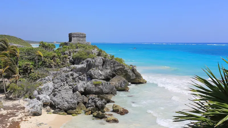 A Maya ruin on a rocky cliff above a turquoise Caribbean beach